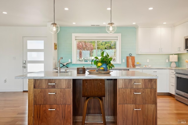 kitchen with white cabinets, light wood-type flooring, light countertops, and a kitchen island with sink