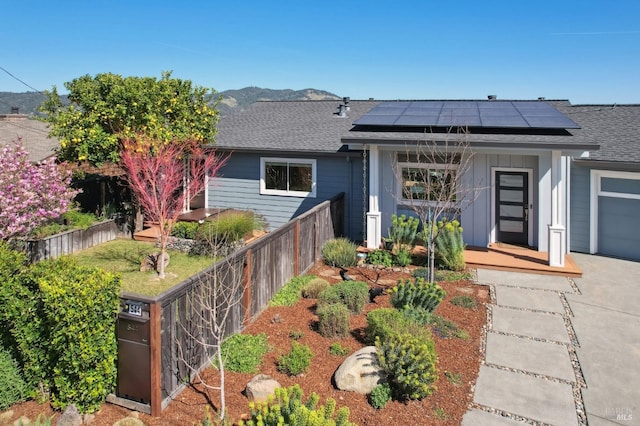 view of front of home with fence, board and batten siding, roof mounted solar panels, and roof with shingles