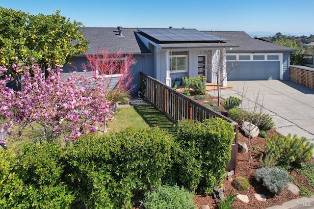 view of front facade with roof mounted solar panels, a garage, driveway, and a shingled roof