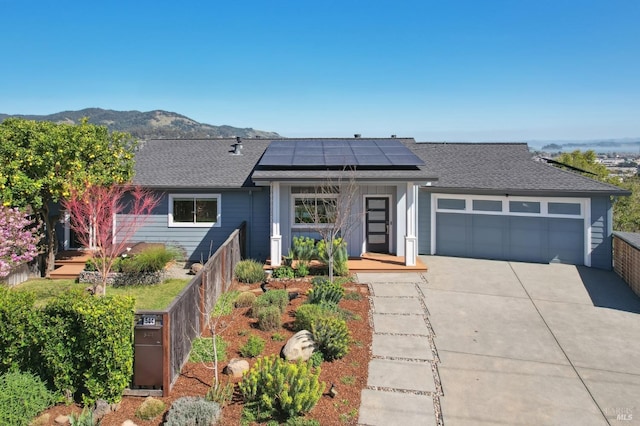 view of front of home featuring roof mounted solar panels, a mountain view, concrete driveway, a shingled roof, and a garage