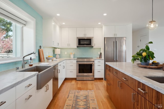 kitchen featuring tasteful backsplash, light wood-type flooring, appliances with stainless steel finishes, hanging light fixtures, and white cabinetry