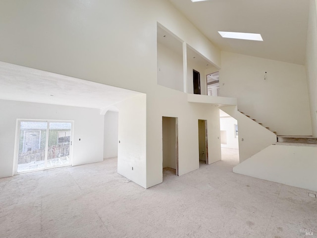 unfurnished living room with stairs, a skylight, arched walkways, and high vaulted ceiling