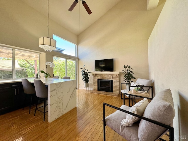 living room featuring a ceiling fan, a brick fireplace, light wood-style floors, and high vaulted ceiling