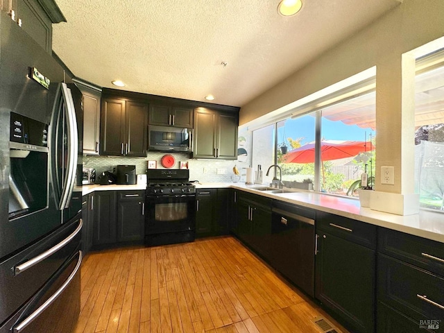 kitchen with light wood finished floors, light countertops, decorative backsplash, black appliances, and a sink