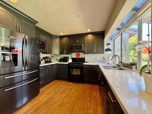 kitchen with a sink, tasteful backsplash, appliances with stainless steel finishes, and light wood-style flooring