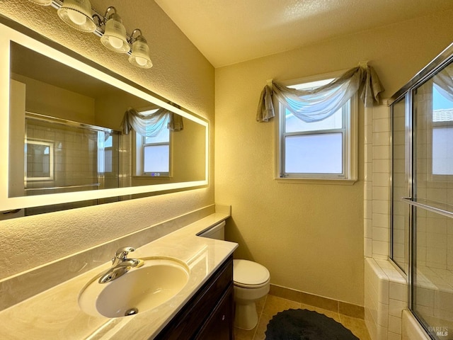 bathroom with toilet, a tile shower, tile patterned flooring, baseboards, and a textured wall