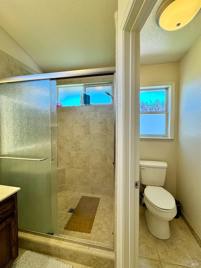 full bath featuring toilet, a stall shower, a textured ceiling, baseboards, and vanity