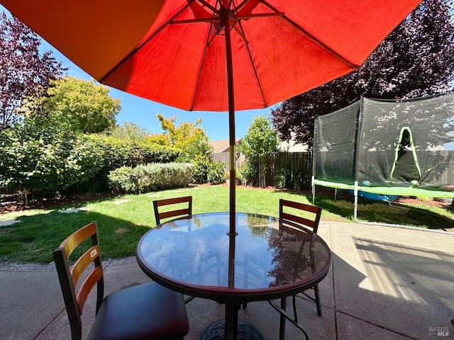 view of patio with outdoor dining space, a trampoline, and fence