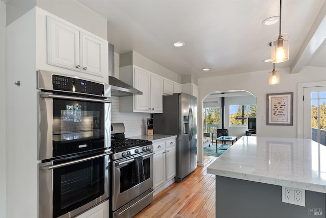 kitchen featuring light stone countertops, arched walkways, appliances with stainless steel finishes, white cabinetry, and backsplash