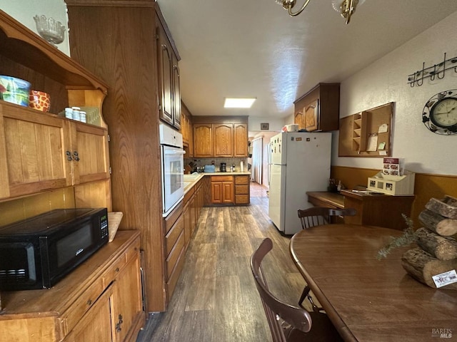kitchen with dark wood finished floors, white appliances, light countertops, and brown cabinetry