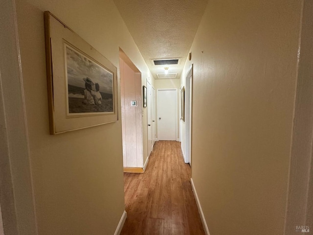 hallway featuring visible vents, a textured ceiling, baseboards, and wood finished floors