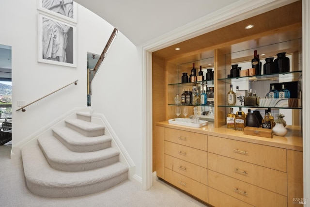 bar featuring a bar, light colored carpet, baseboards, and stairs