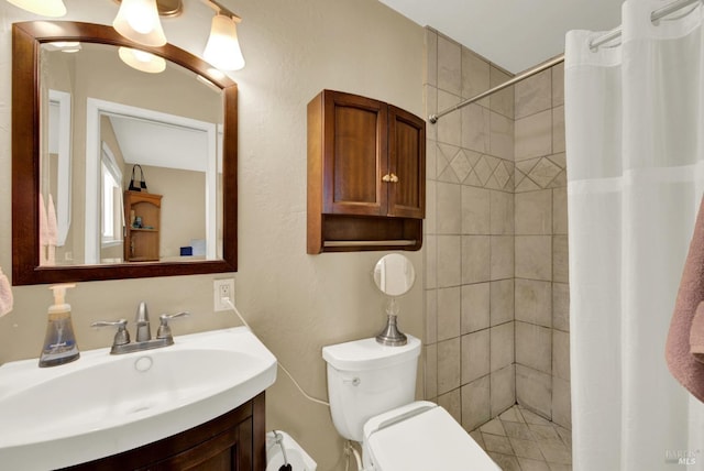 bathroom with toilet, tiled shower, and vanity