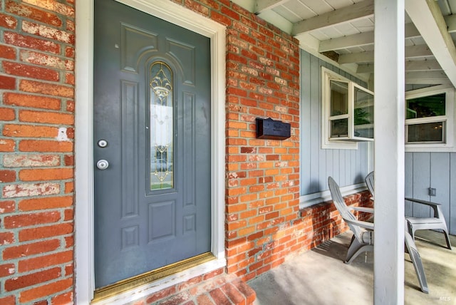 entrance to property featuring a porch and brick siding