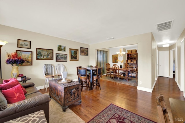 living area with a chandelier, visible vents, baseboards, and wood finished floors