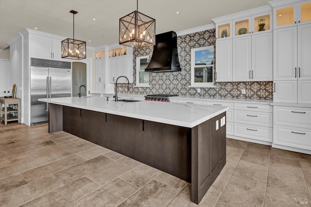 kitchen with crown molding, range hood, an inviting chandelier, a sink, and built in fridge