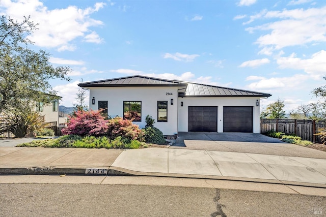 view of front of home with stucco siding, a garage, a standing seam roof, metal roof, and fence