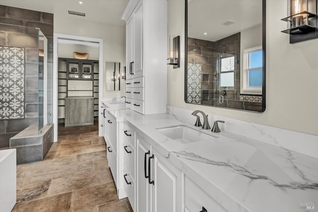 bathroom featuring visible vents, tiled shower, vanity, and stone finish flooring