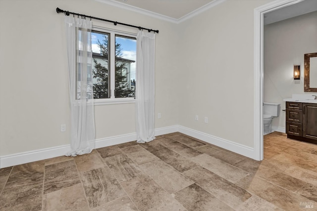 spare room featuring crown molding, stone finish floor, a sink, and baseboards