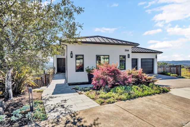 contemporary house with fence, concrete driveway, stucco siding, and a standing seam roof