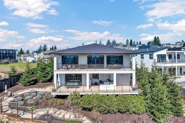 rear view of house featuring a balcony, stucco siding, a standing seam roof, metal roof, and fence