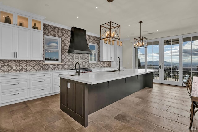 kitchen with exhaust hood, a sink, light countertops, a chandelier, and a kitchen island with sink