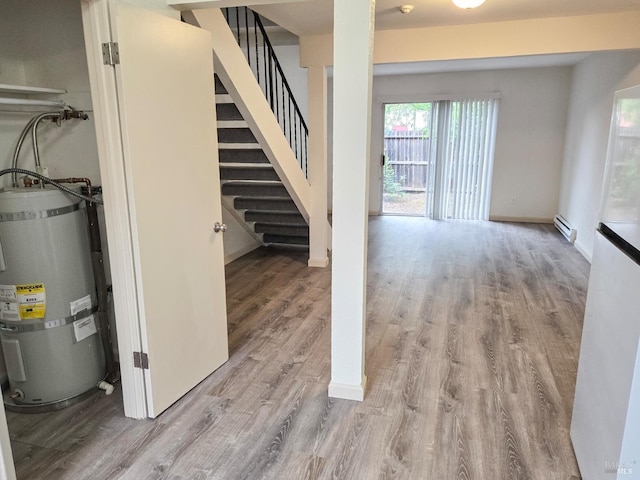 below grade area with stairway, a baseboard radiator, strapped water heater, baseboards, and wood finished floors