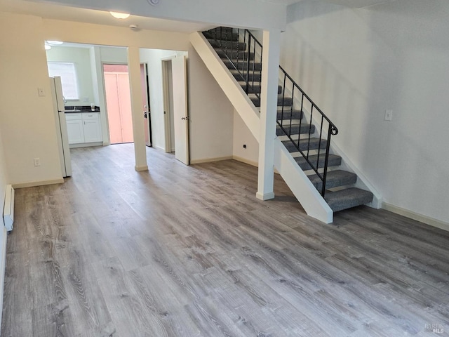 below grade area featuring baseboards, wood finished floors, and freestanding refrigerator