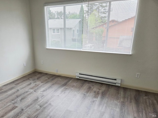 empty room featuring wood finished floors, a healthy amount of sunlight, a baseboard heating unit, and baseboards