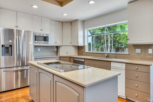 kitchen with appliances with stainless steel finishes, a center island, decorative backsplash, light wood finished floors, and a sink