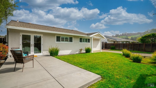 rear view of house featuring fence, a lawn, french doors, and stucco siding