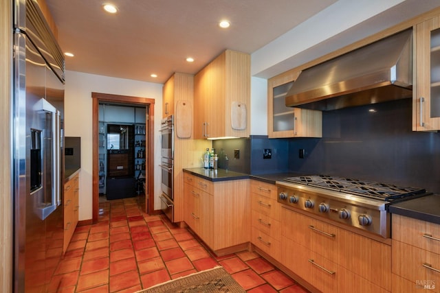 kitchen with dark countertops, light brown cabinets, decorative backsplash, stainless steel appliances, and wall chimney exhaust hood