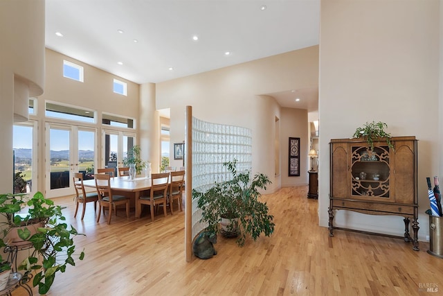 dining room with french doors, a healthy amount of sunlight, a towering ceiling, and light wood finished floors