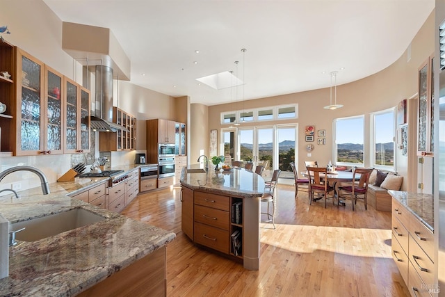 kitchen with a sink, stainless steel gas cooktop, light wood-type flooring, and island range hood