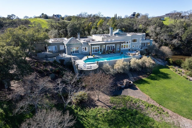 back of property with stucco siding, a chimney, a yard, a patio area, and an outdoor pool