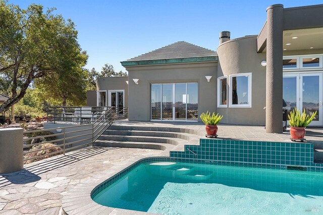 rear view of house with a patio, an outdoor pool, and stucco siding