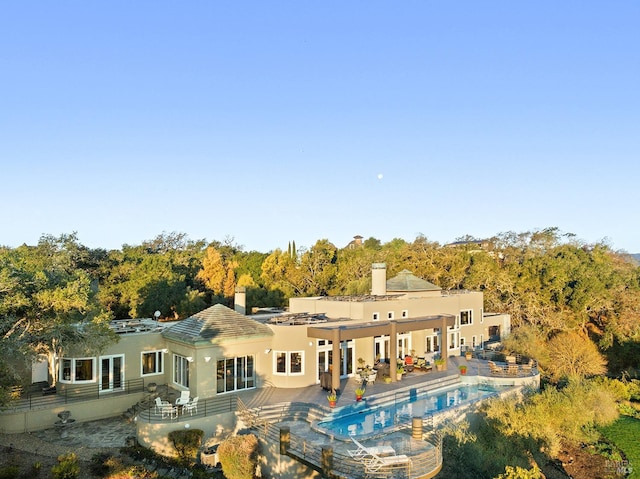 rear view of property featuring a patio, fence, an outdoor pool, and stucco siding