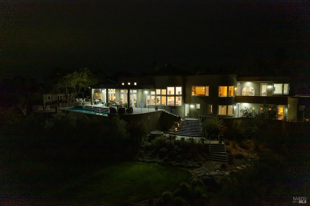 back of house at twilight featuring stairway and an outdoor pool
