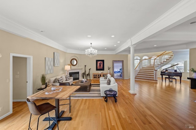 living room with stairway, light wood finished floors, ornamental molding, decorative columns, and a glass covered fireplace
