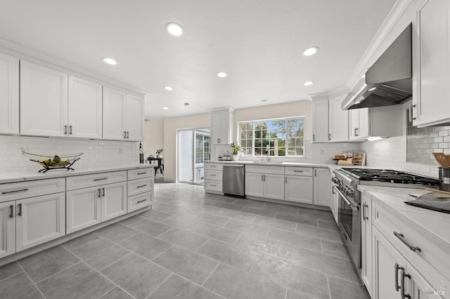 kitchen with recessed lighting, stainless steel appliances, backsplash, a sink, and wall chimney exhaust hood