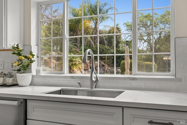 interior details featuring white cabinets, dishwasher, a sink, light stone countertops, and tasteful backsplash