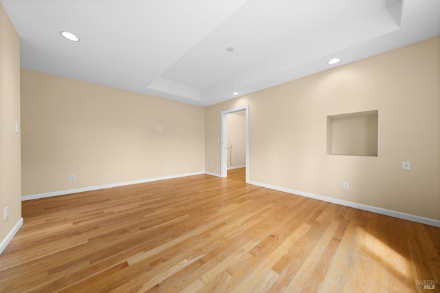 spare room featuring light wood-type flooring, baseboards, a tray ceiling, and recessed lighting