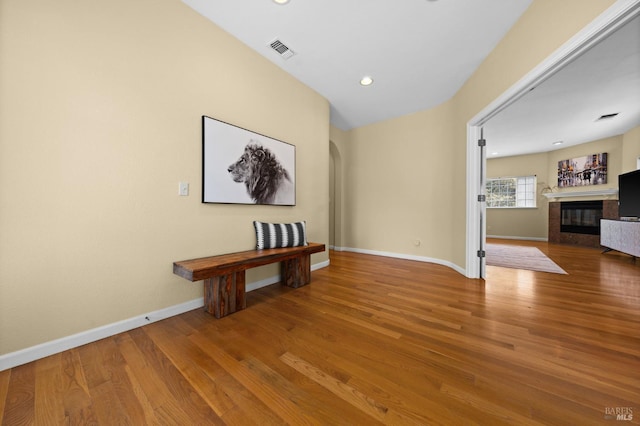 interior space with arched walkways, baseboards, visible vents, wood finished floors, and a tile fireplace