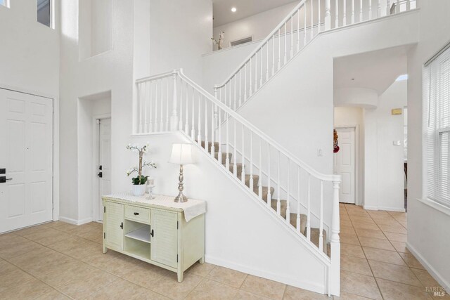 staircase featuring tile patterned flooring, baseboards, and a towering ceiling