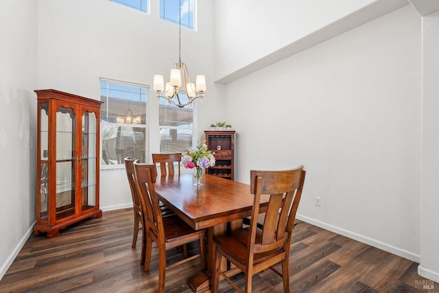 dining area with dark wood-style floors, a notable chandelier, a high ceiling, and baseboards