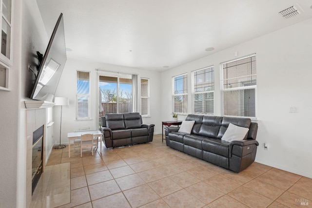 living room with a glass covered fireplace, light tile patterned floors, baseboards, and visible vents