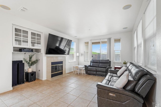 living area featuring light tile patterned floors, visible vents, a tiled fireplace, and baseboards