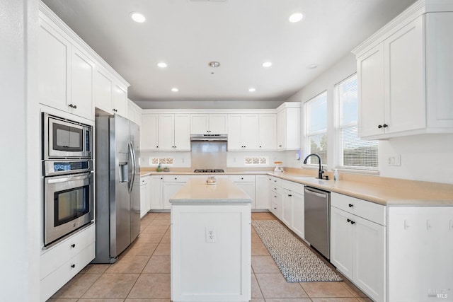 kitchen with a kitchen island, under cabinet range hood, stainless steel appliances, light tile patterned flooring, and white cabinetry