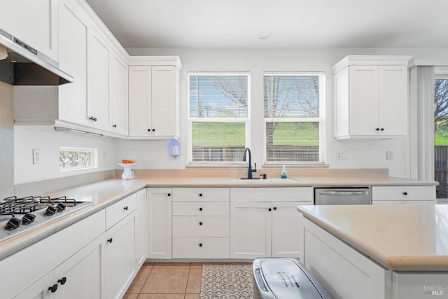 kitchen featuring light tile patterned floors, a sink, white cabinets, under cabinet range hood, and appliances with stainless steel finishes