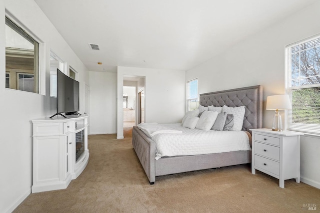 bedroom with ensuite bath, light colored carpet, visible vents, and baseboards